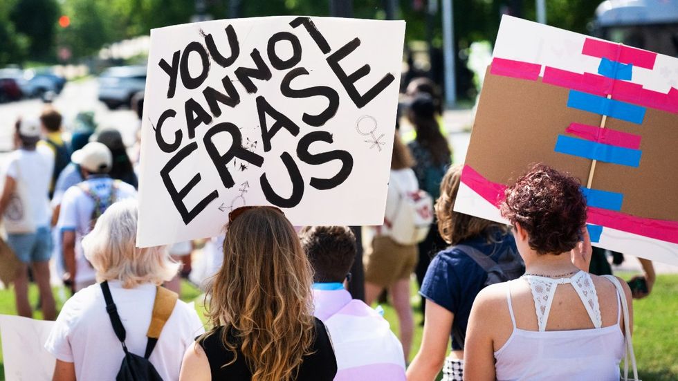 A protester holds a sign that reads you cannot erase us